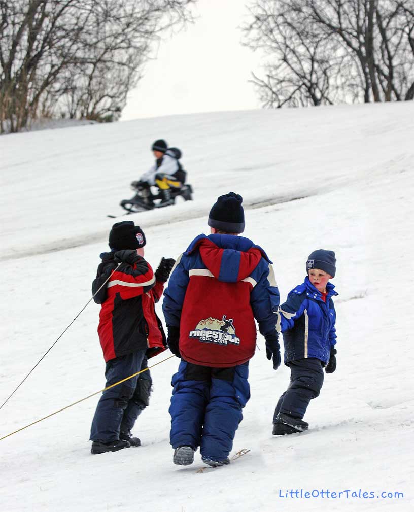 three boys pulling snow sled up hill